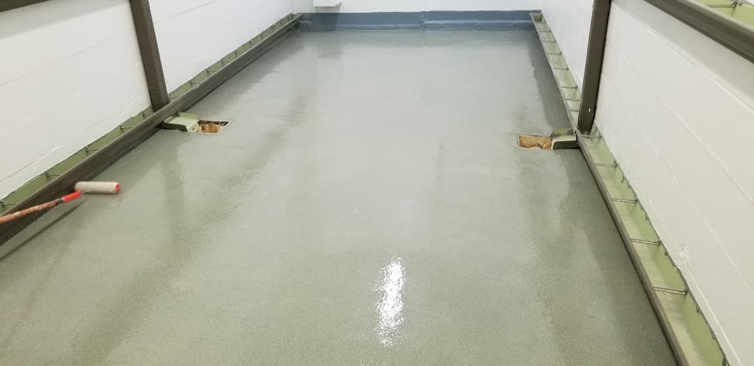 Newly poured concrete floor in a hallway with aroller on the side for finishing touches.