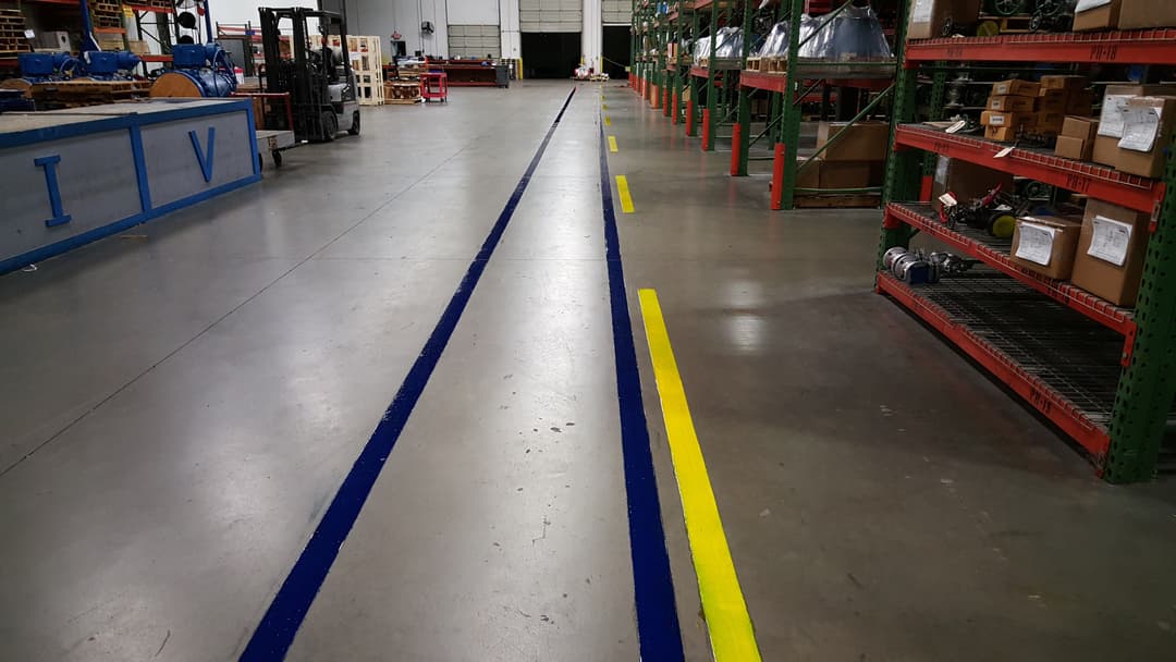 Warehouse floor with blue and yellow lane markings, shelving units, and equipment in view.