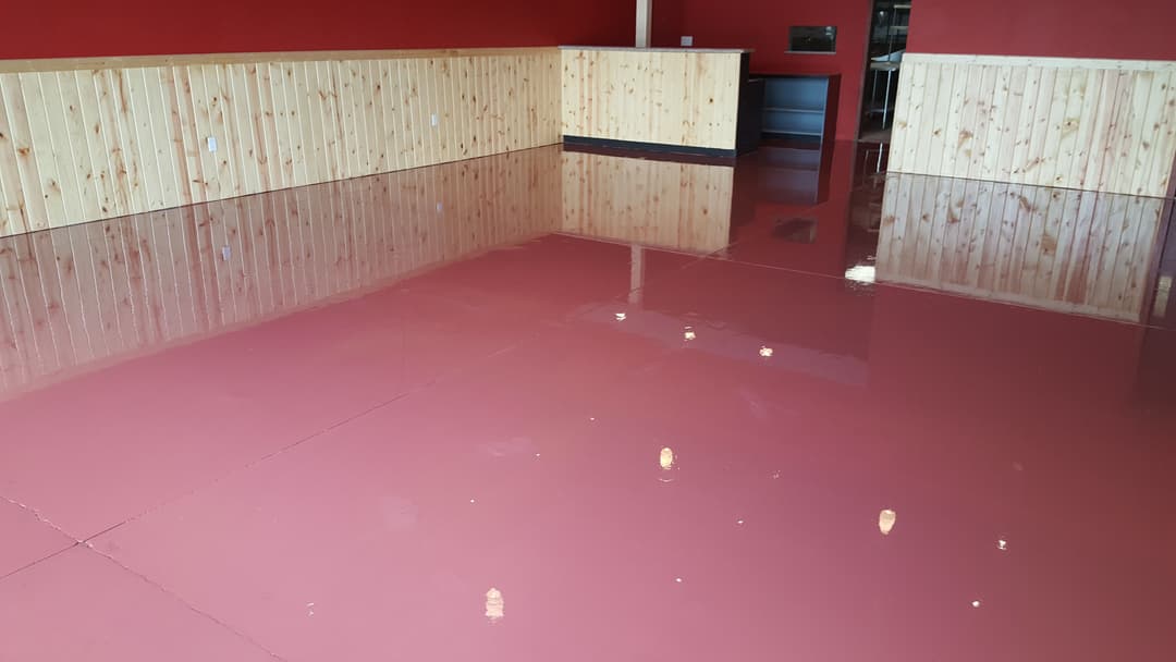 Shiny red epoxy floor in a room with wooden wall panels and minimal furnishings.