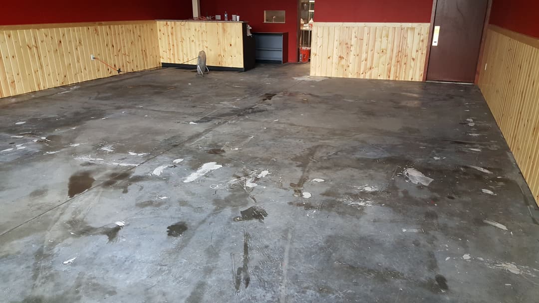 Empty room with stained concrete floor and wooden paneling, ready for renovation.