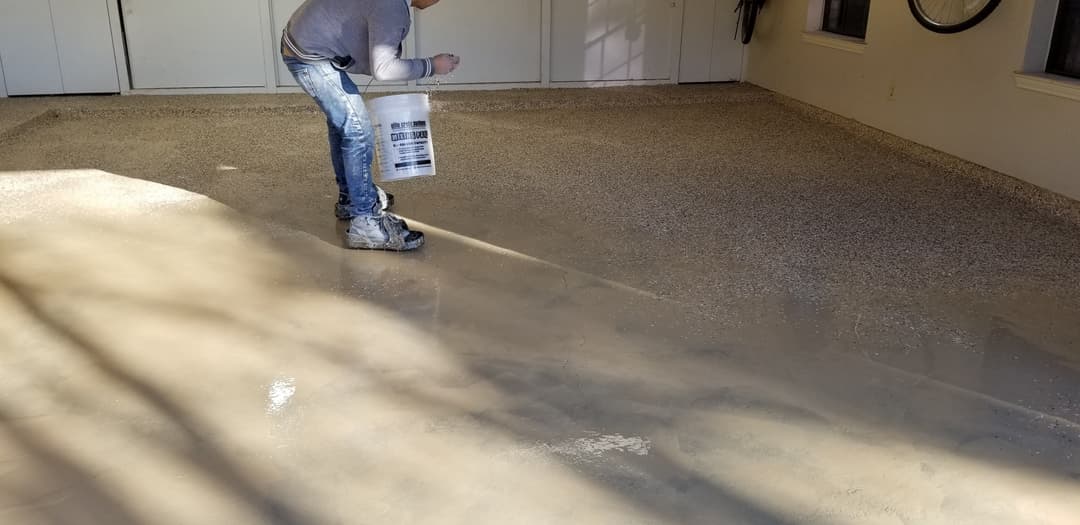 Person applying epoxy flooring in a garage, showcasing a smooth, shiny surface.
