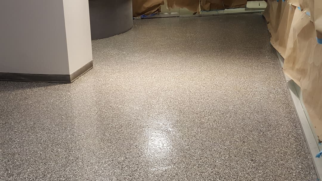Shiny epoxy floor with a gray speckled finish in a partially completed interior space.