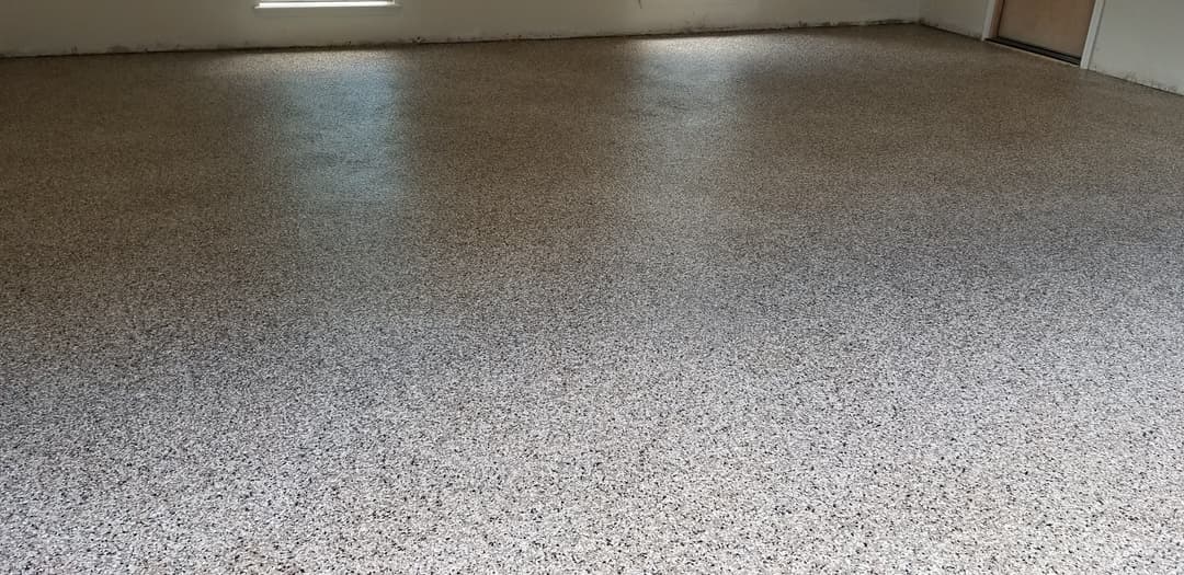 Newly installed epoxy floor in a well-lit empty room with a speckled surface.