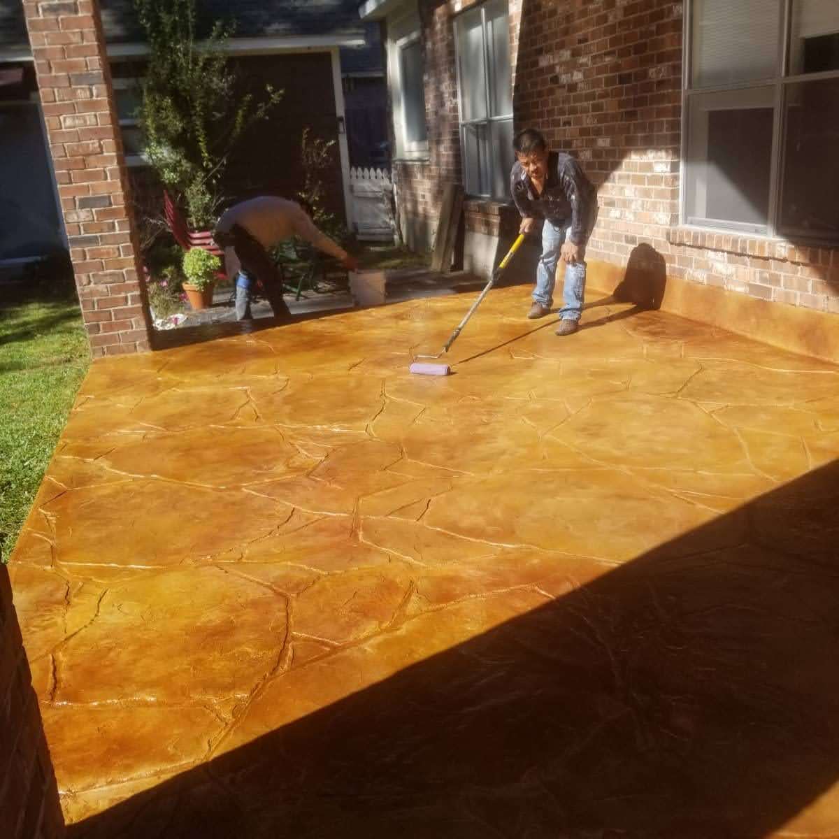 Workers applying a decorative concrete finish on a patio with a roller.