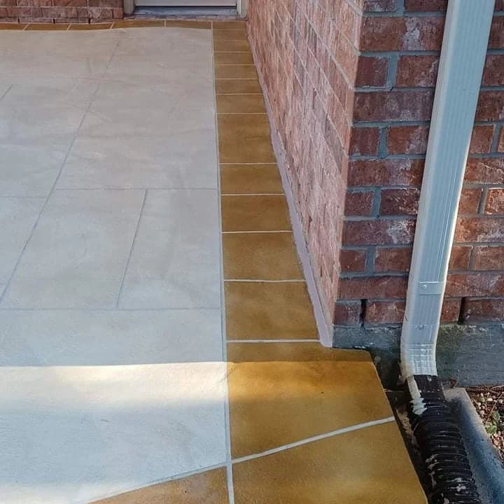 Newly finished concrete patio with textured design adjacent to brick wall and downspout.