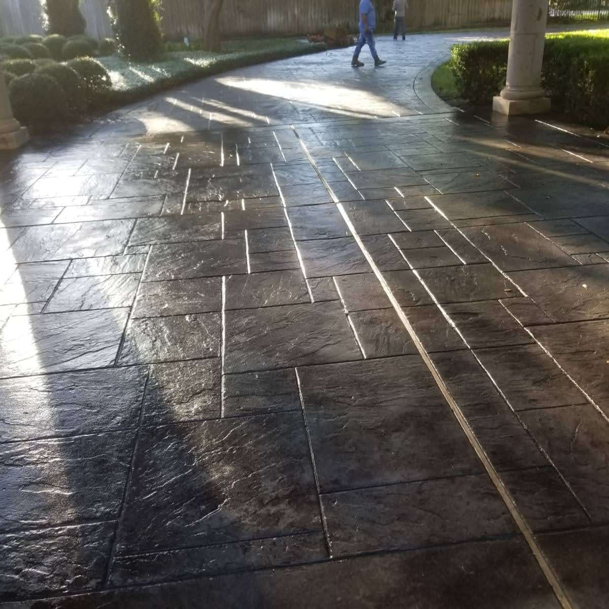 Footpath with textured concrete, sunlight casting long shadows, and two people walking.