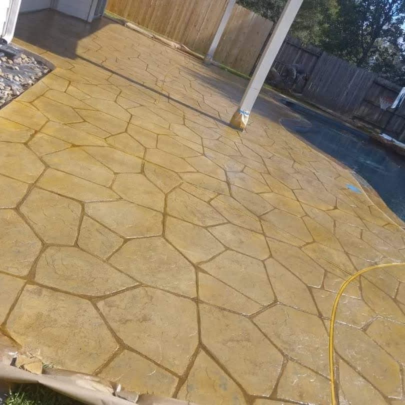 Stained concrete patio with a flagstone pattern near a pool and wooden fence.