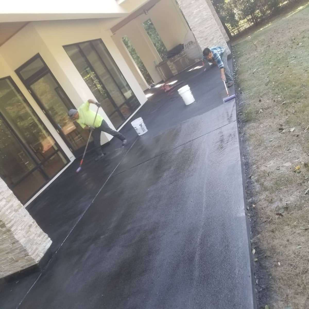 Workers applying sealant on a newly finished concrete patio outside a modern home.