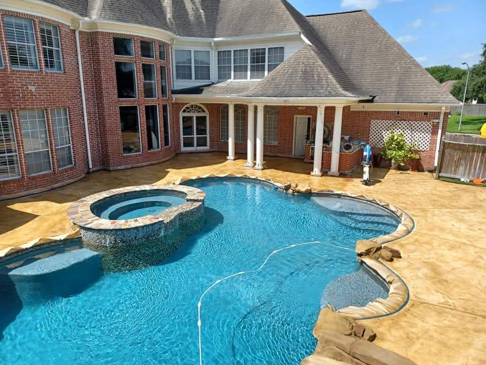 Luxury backyard pool with spa, decorative stamped concrete, and brick home exterior.
