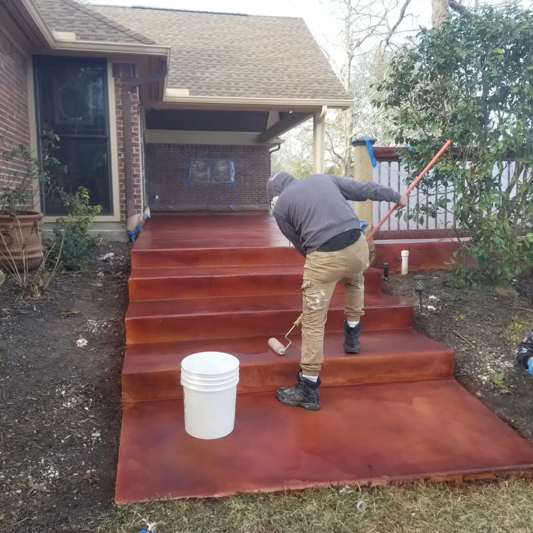 Person applying a red stain to concrete steps in a residential outdoor setting.