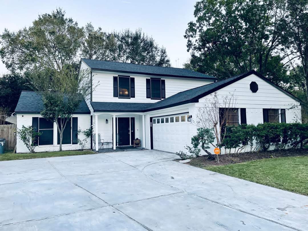 Two-story white house with black roof, large driveway, and green landscaping.