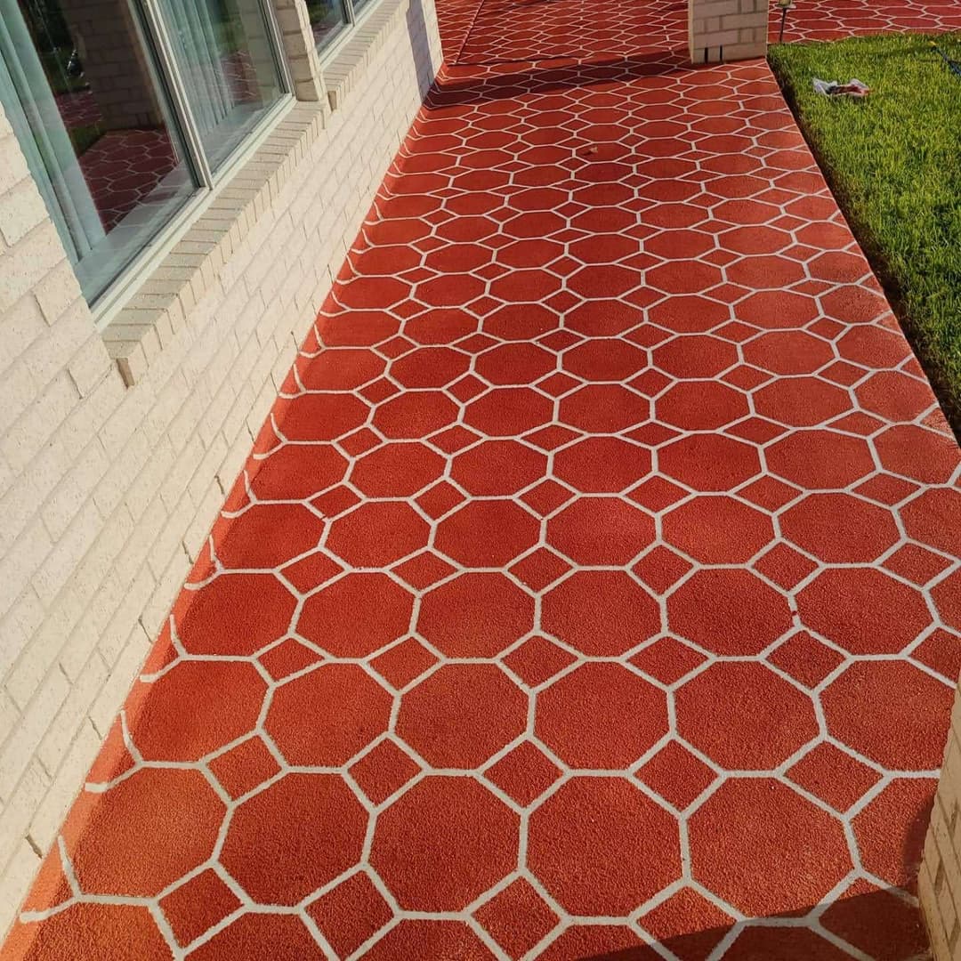 Red hexagonal patterned pavement with white grout, bordered by grass and a brick wall.
