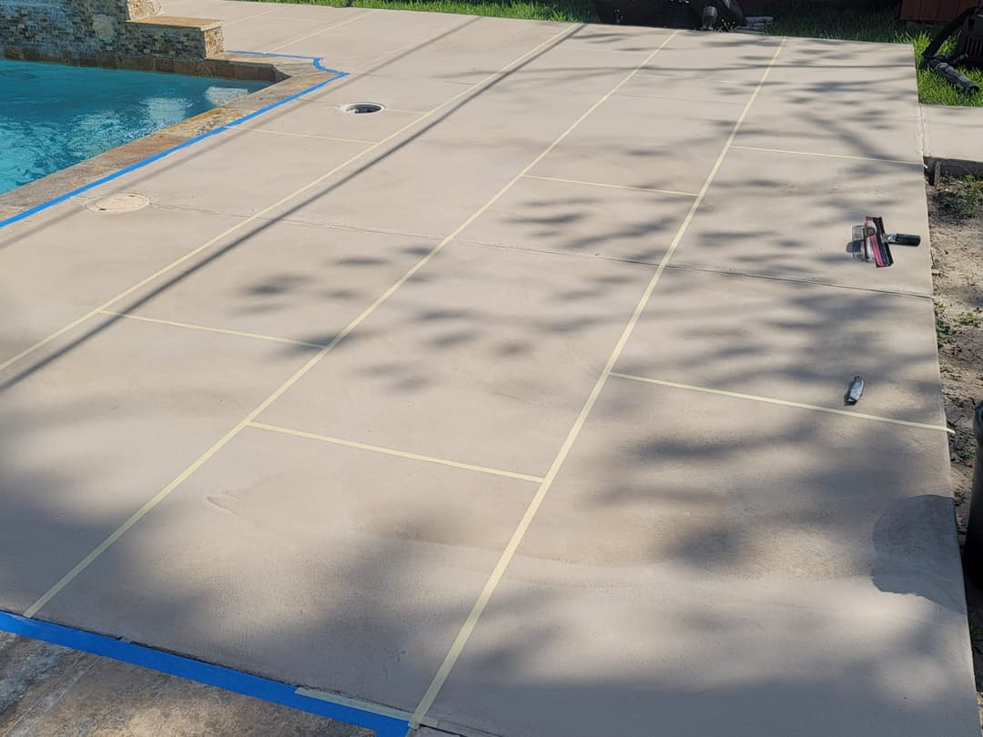 Freshly marked concrete patio with blue tape, ready for sealing near a swimming pool.