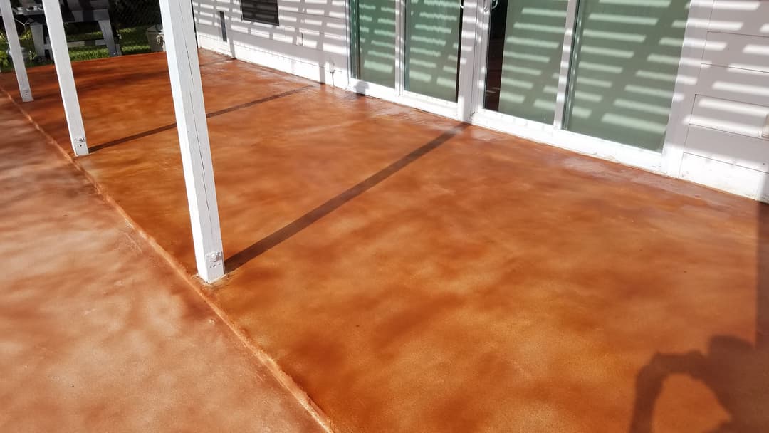 Freshly stained concrete patio with warm brown tones, shadows from overhead structure.
