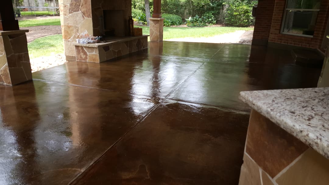 Polished stained concrete patio with standing stone accents and green landscaping in background.