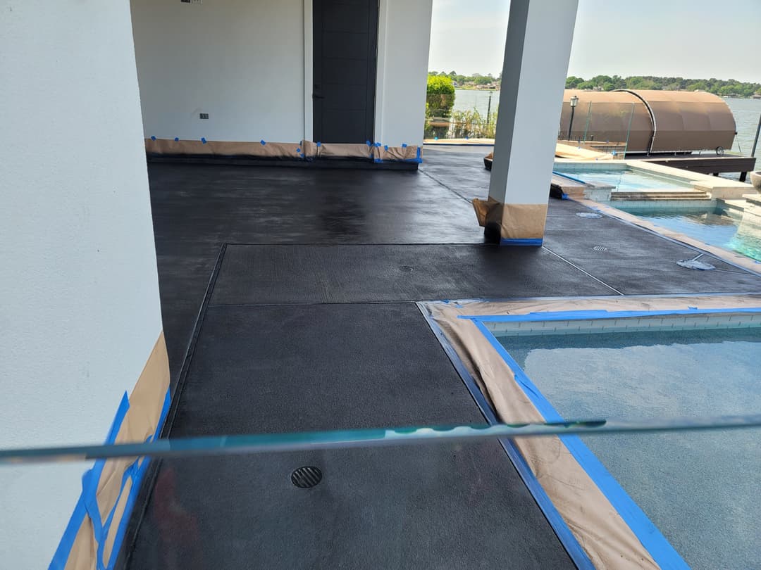 Newly laid black concrete patio near a pool, freshly taped for finishing touches.