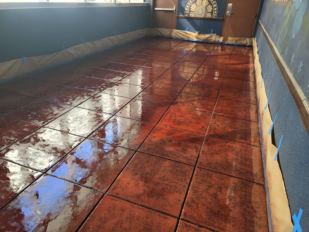 Glossy red stained tile floor with masking tape along edges in a well-lit interior space.