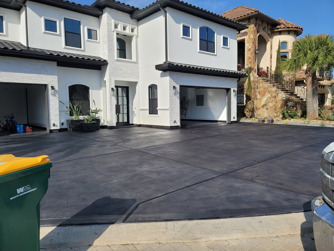 Modern two-story home with a black driveway, green garbage bin, and sunny landscaping.