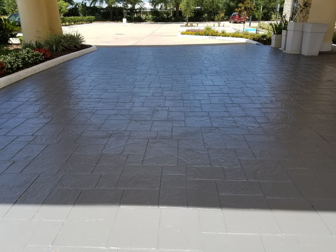 Gray stamped concrete flooring in a sunny entrance area with landscaped surroundings.
