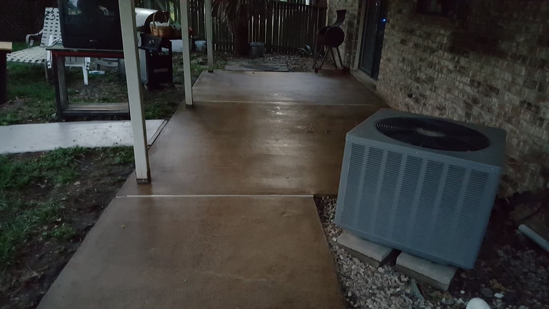 Concrete patio with an air conditioning unit beside a brick house in a backyard setting.