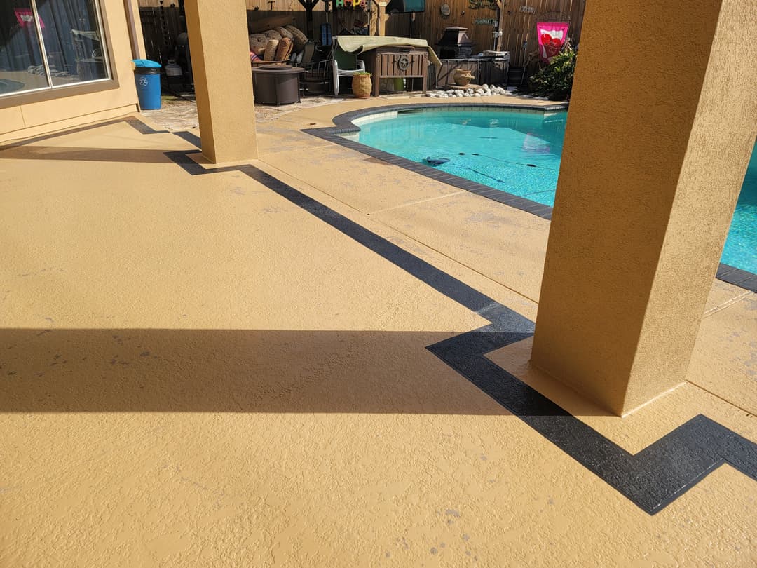 Poolside patio with tan surface and black geometric border, featuring columns and lounge area.