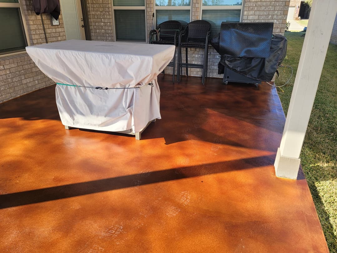 Patio with stained concrete flooring, a covered table, and outdoor furniture in sunlight.