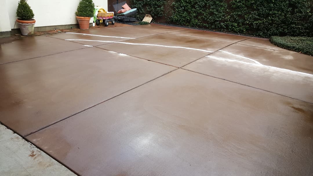 Newly sealed concrete patio with clean lines, potted plants, and garden tools.