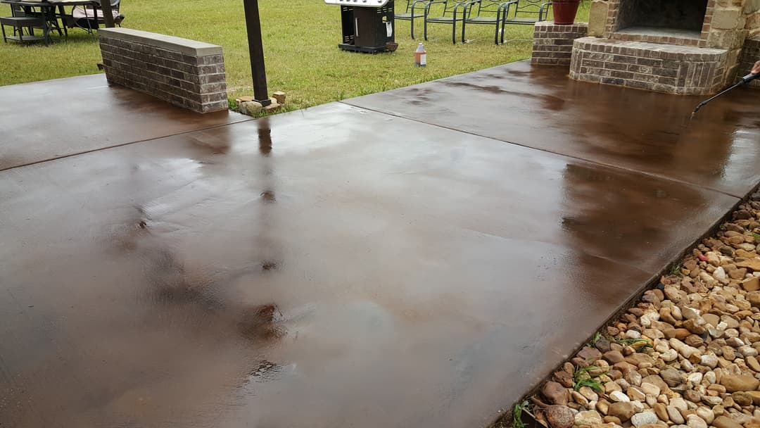 Freshly sealed concrete patio with polished finish and decorative rock border.