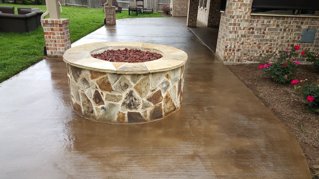 Stone fire pit on a polished concrete patio with flowers and green lawn in the background.