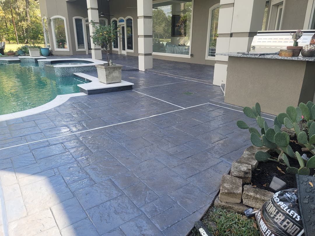 Stamped concrete patio by a pool with greenery and decorative potted plants.