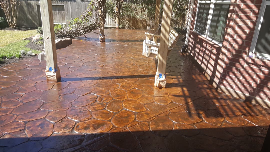 Decorative stamped concrete patio with polished finish and covered seating area in a sunny backyard.