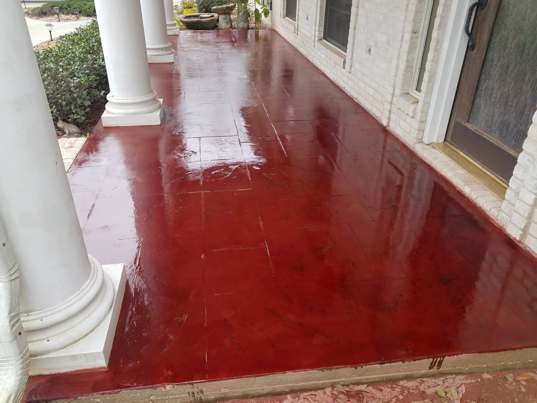 Glossy red stained concrete porch with decorative stamping and white columns.