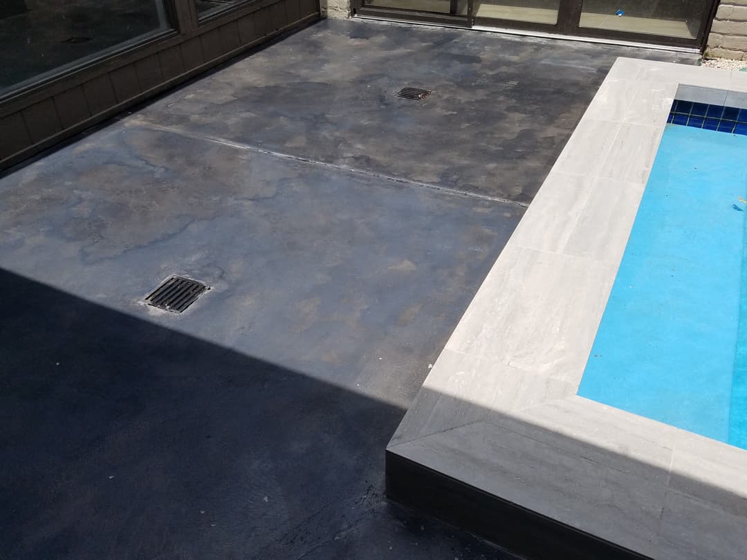 Renovated concrete pool deck with drainage and blue swimming pool water.