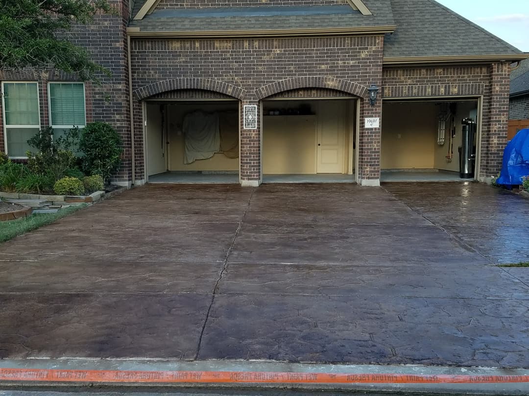 Stamped concrete driveway with two garage doors and neatly landscaped front yard.