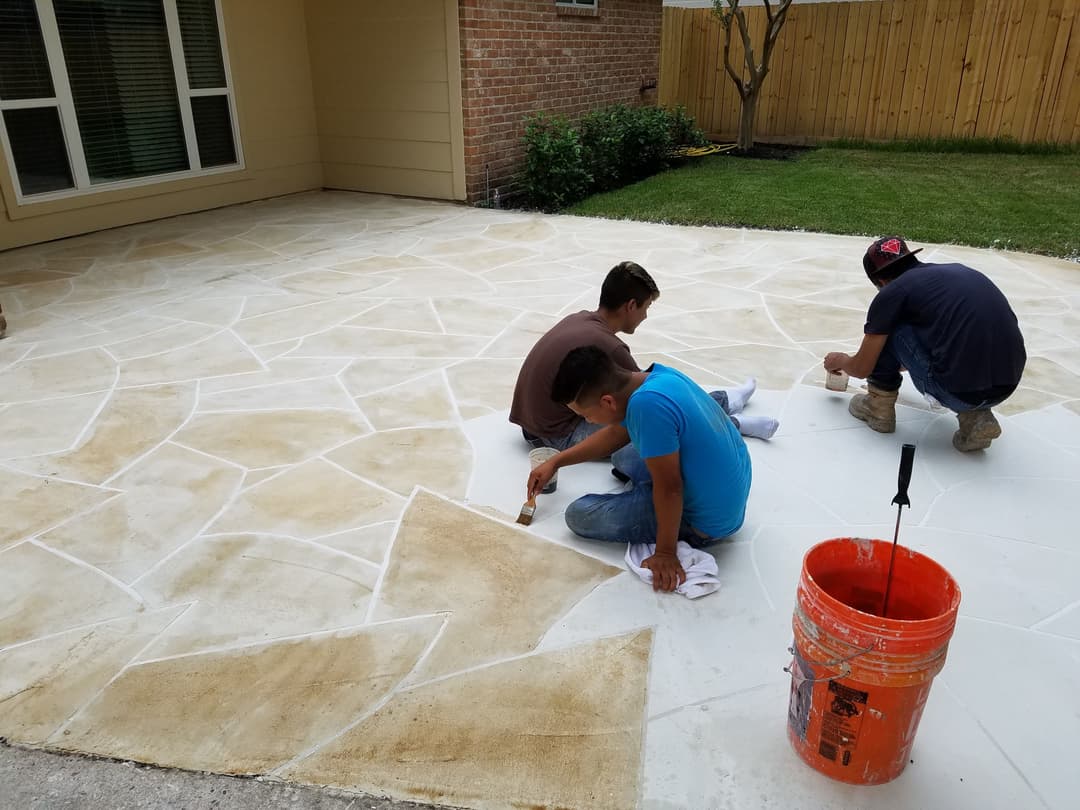 Workers applying a decorative finish to a stone patio in a residential backyard.