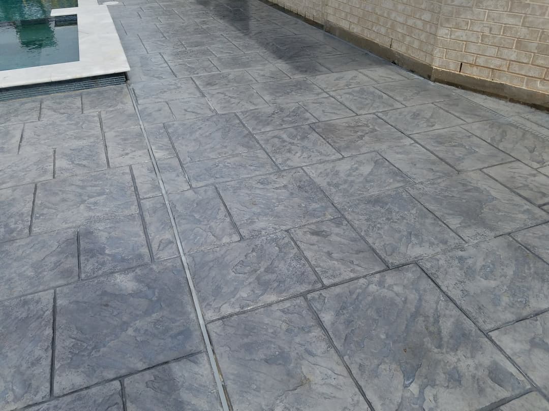 Textured gray stamped concrete patio surrounding a swimming pool with a modern design.