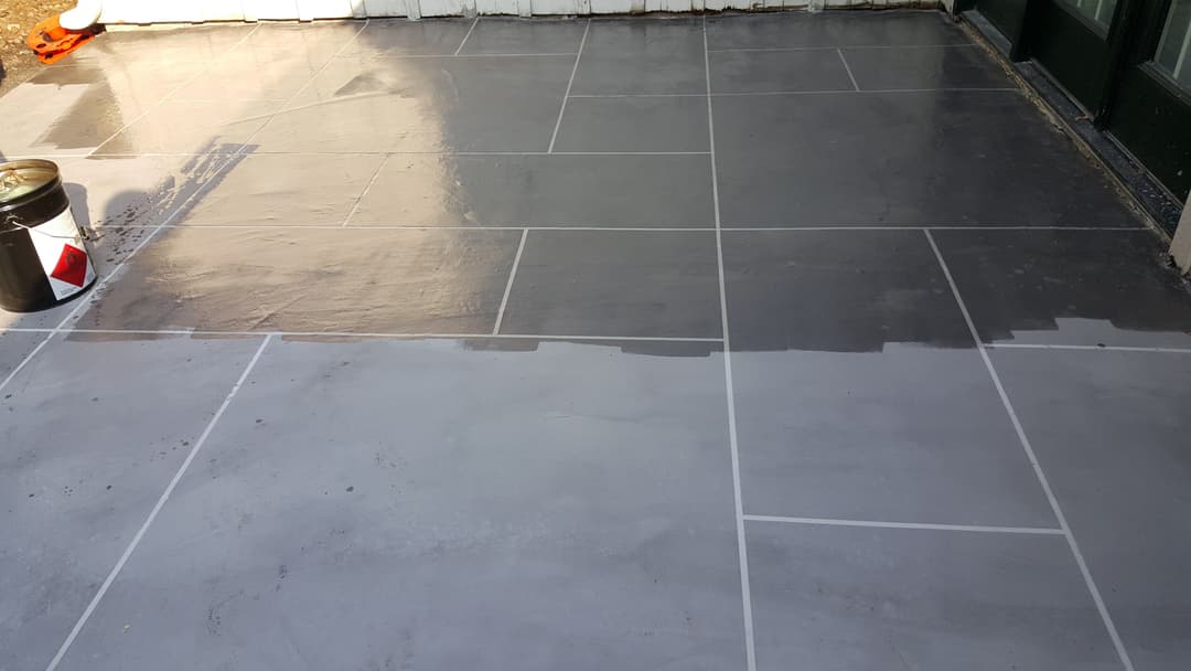 Gray tile floor being painted, showcasing half finished glossy surface with tools nearby.