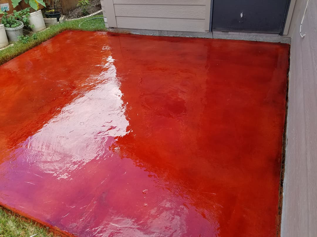 Glossy red concrete patio surface beside a house, reflecting light and enhancing outdoor space.
