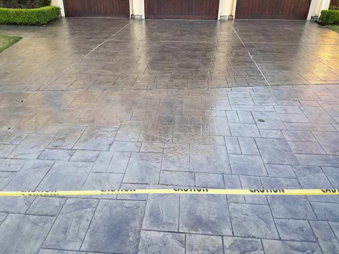 Freshly sealed stamped concrete driveway with caution tape marking off the area.