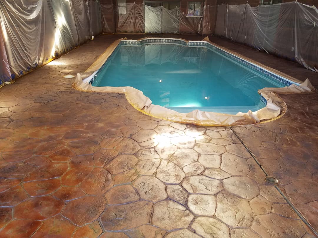 Indoor swimming pool with blue water and decorative stamped concrete flooring under construction.