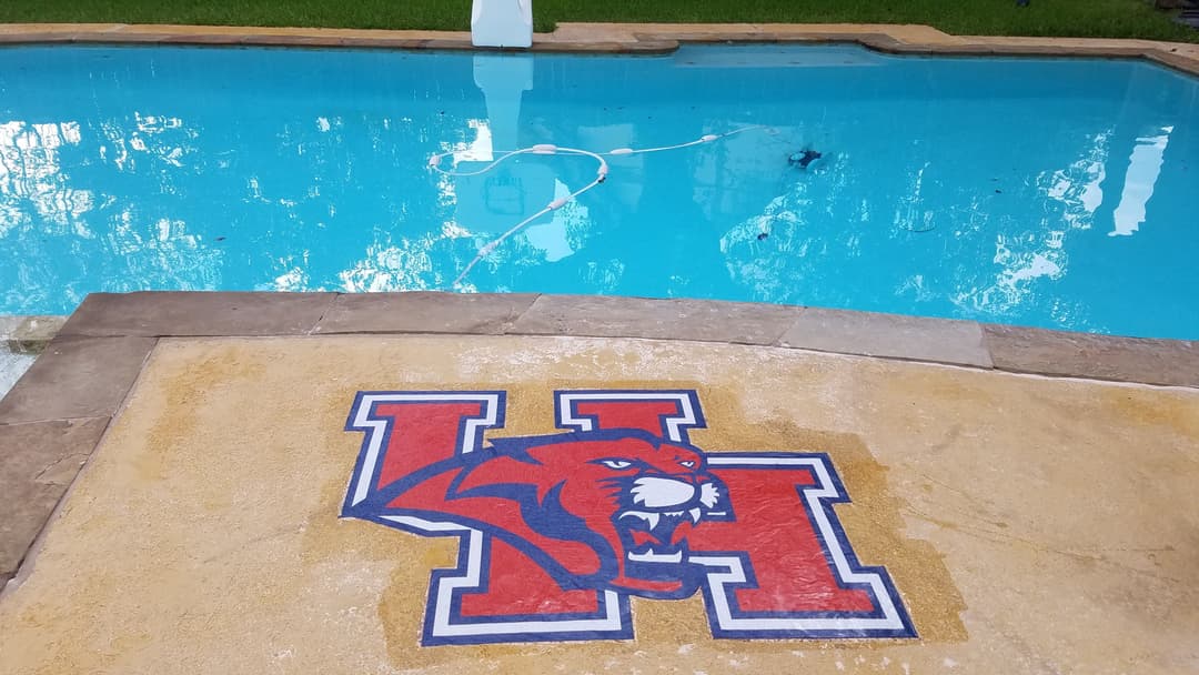 Poolside view featuring a painted University of Houston logo on a stone surface.