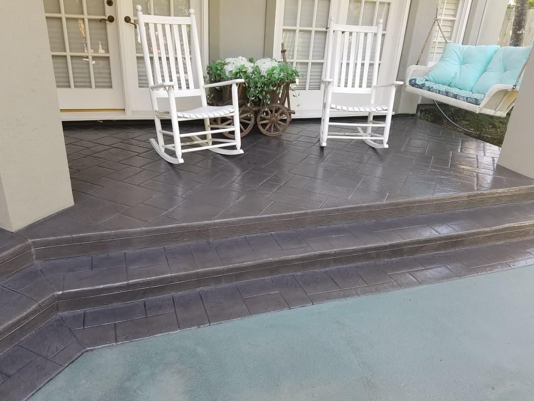 Stylish porch with two rocking chairs, potted plants, and a decorative swing on stamped concrete.