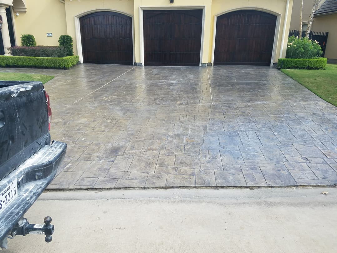 Decorative stamped concrete driveway with dark wooden garage doors and edged landscaping.