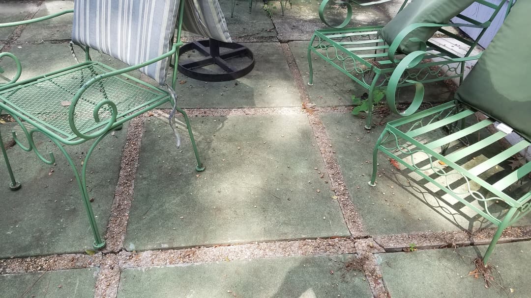 Green metal chairs on a stone patio, with shadows and scattered leaves. Outdoor seating area.