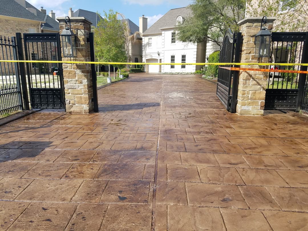 Gated entrance with stone pillars and a stained concrete driveway, marked with caution tape.
