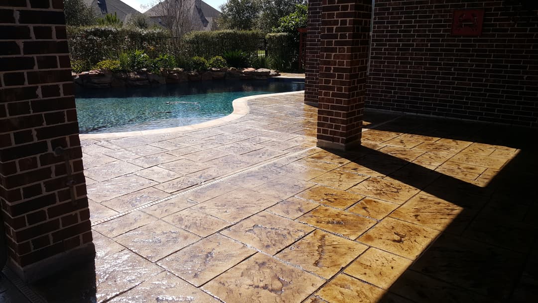 Outdoor pool area with stamped concrete, sunny landscaping, and stone accents.