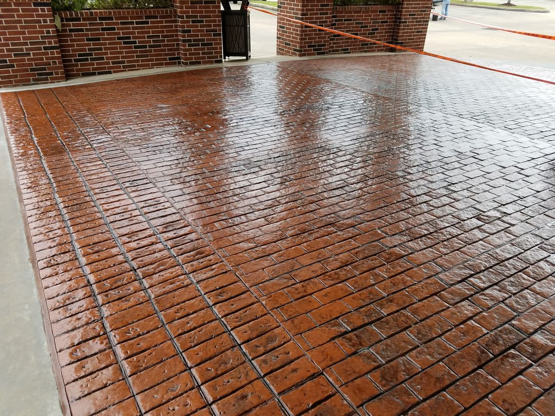Wet stamped concrete surface with a brick pattern, showcasing rich brown tones and a glossy finish.