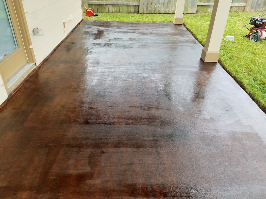 Freshly stained brown concrete patio with a clean, glossy finish and green grass in background.