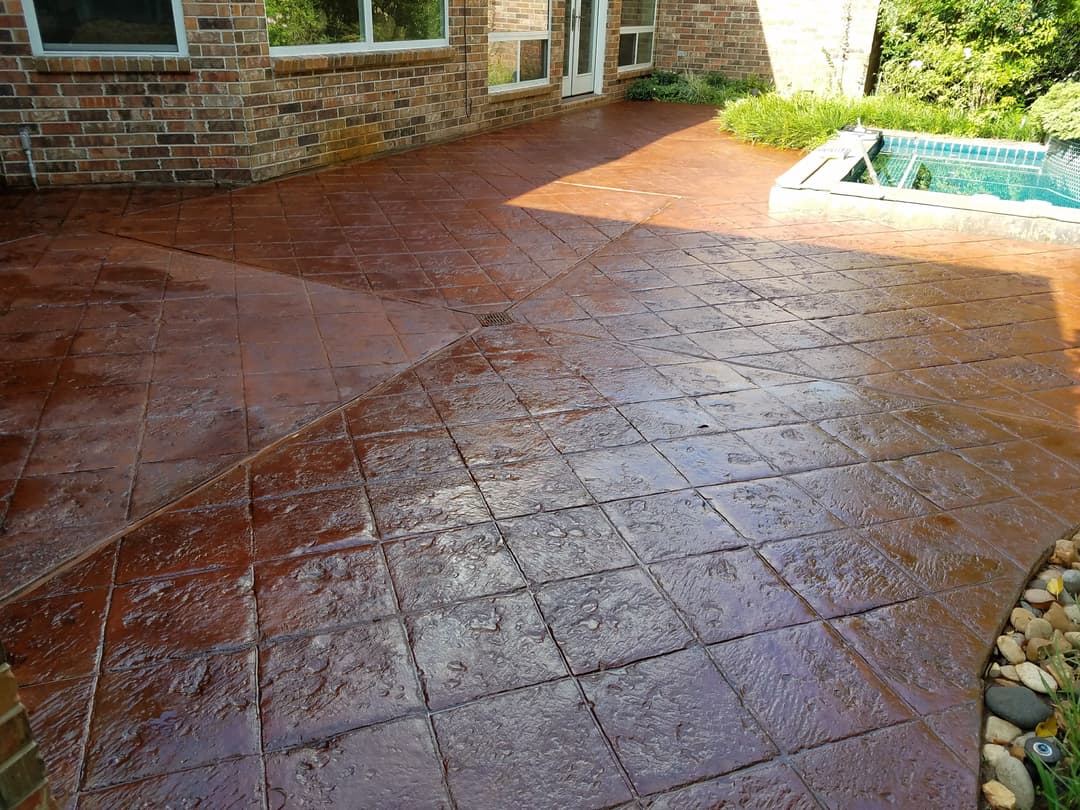 Stamped concrete patio with a glossy finish, surrounded by greenery and a pool area.