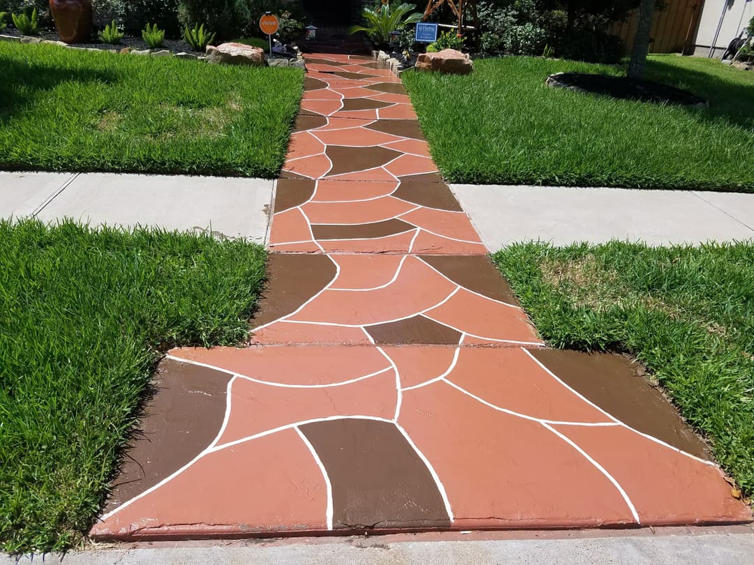 Decorative concrete walkway design with brown and orange hues in a landscaped yard.